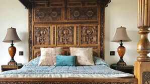 A bed with a wooden headboard featuring intricate carvings, flanked by two nightstands with lamps, and a patterned bedspread. - Loftsome Bridge Hotel (Selby)