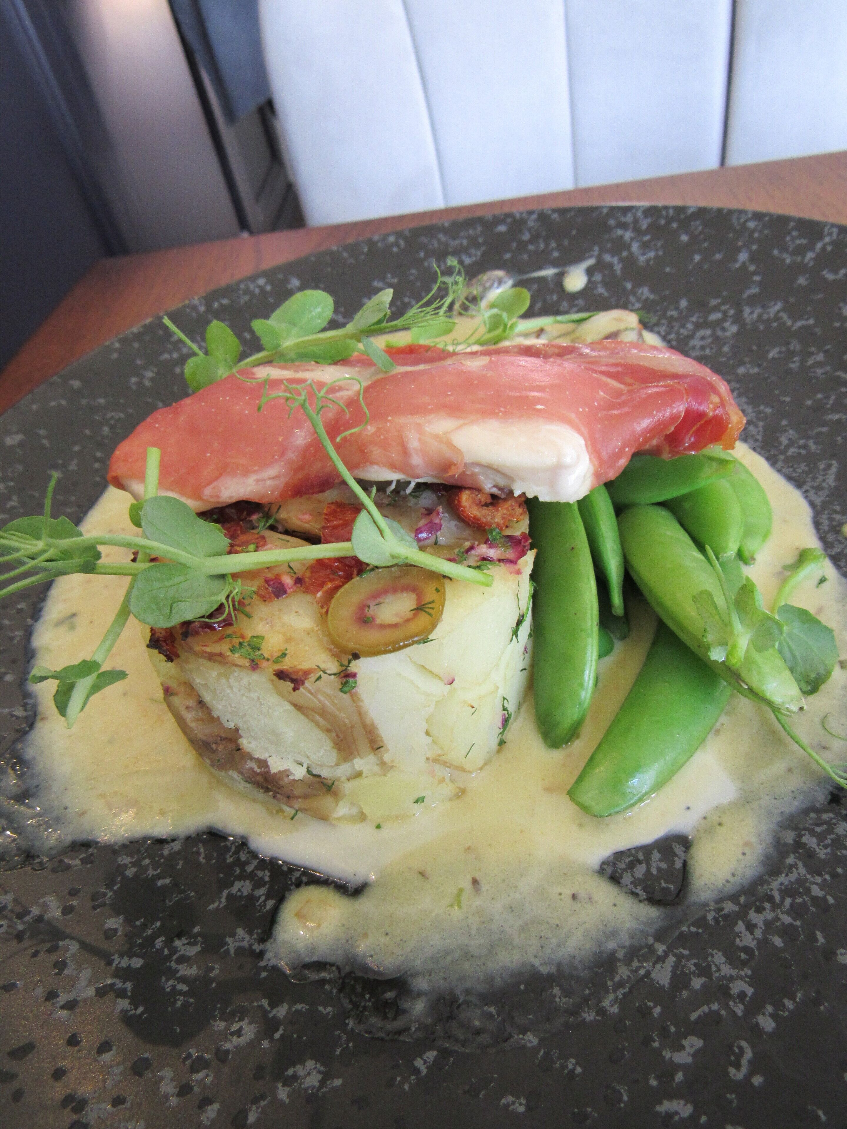 A plate of food with a piece of fish, green peas, and a slice of meat on top.