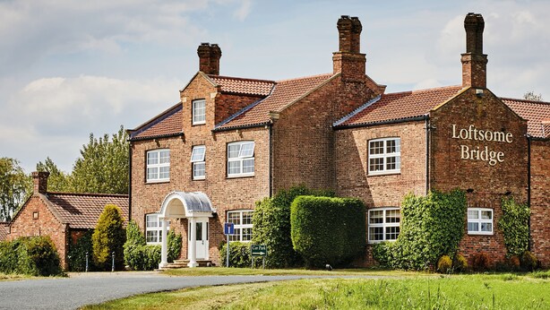 A brick building with the name "Loxton Bridge" on the side, featuring a traditional design with multiple chimneys and a well-maintained lawn. - Loftsome Bridge Hotel (Selby)