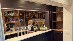 A bar area with a counter, shelves of liquor bottles, and a person working behind the bar. - Loftsome Bridge Hotel (Selby)