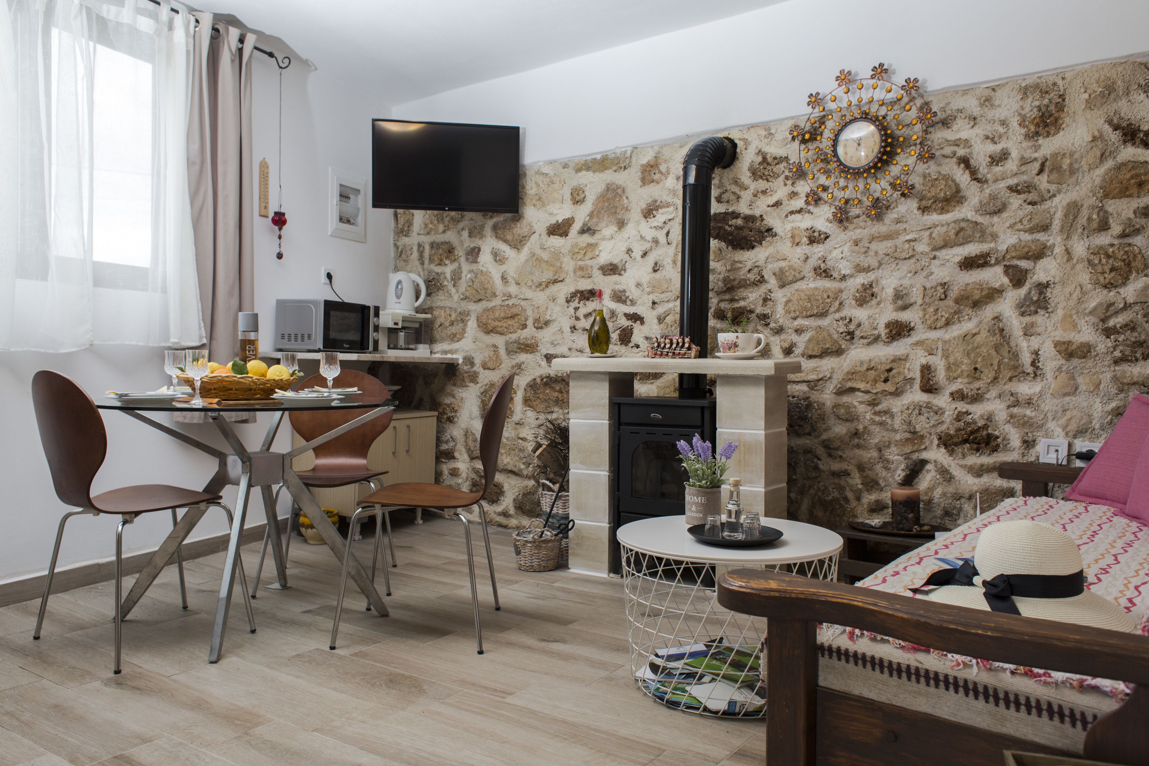 Un salon chaleureux avec un mur en pierre, une cheminée, un coin repas avec des chaises et un téléviseur fixé au mur.