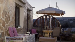 A stone building with a stone bench, a table, chairs, and an umbrella. - Mylos (Kissamos)