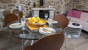 A dining area with a glass table, chairs, and a basket of fruit. A fireplace is visible in the background. - Mylos (Kissamos)