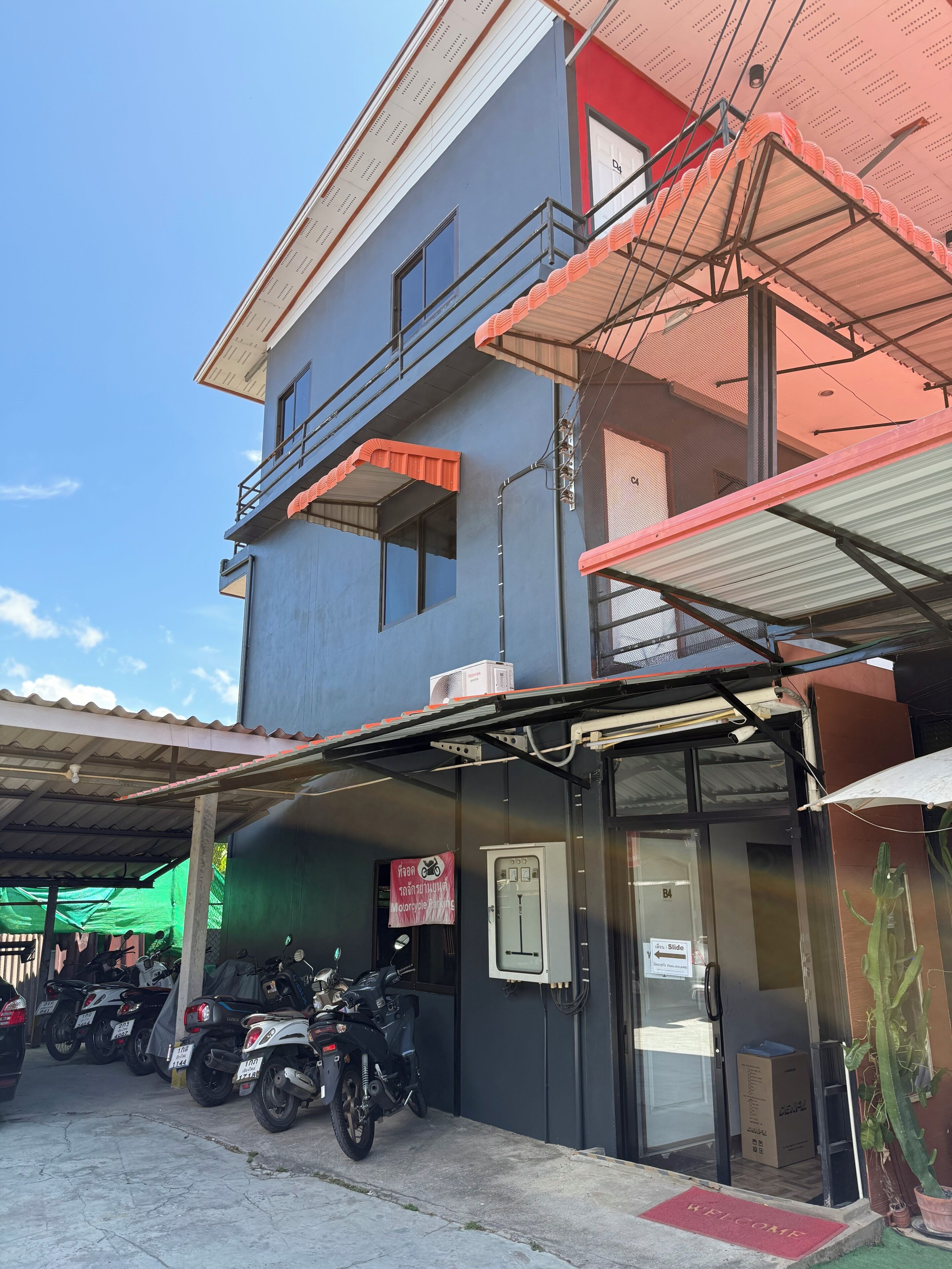 A multi-story building with a covered parking area, a motorcycle rental service, and a door with a sign.