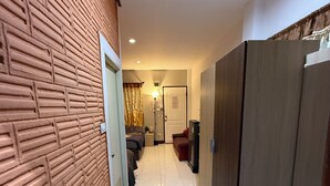 A hallway with a brick wall, a door, a bed, a wardrobe, and a trash bin. - Sandee Place Mountain View Chomthong (Chom Thong)