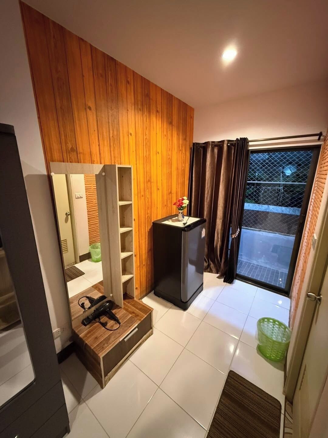 Ein gemütlicher Raum mit einer Holzvertäfelung, einem kleinen schwarzen Kühlschrank, einem Holzkasten, einem Spiegel und einer Glastür zum Außenbereich.