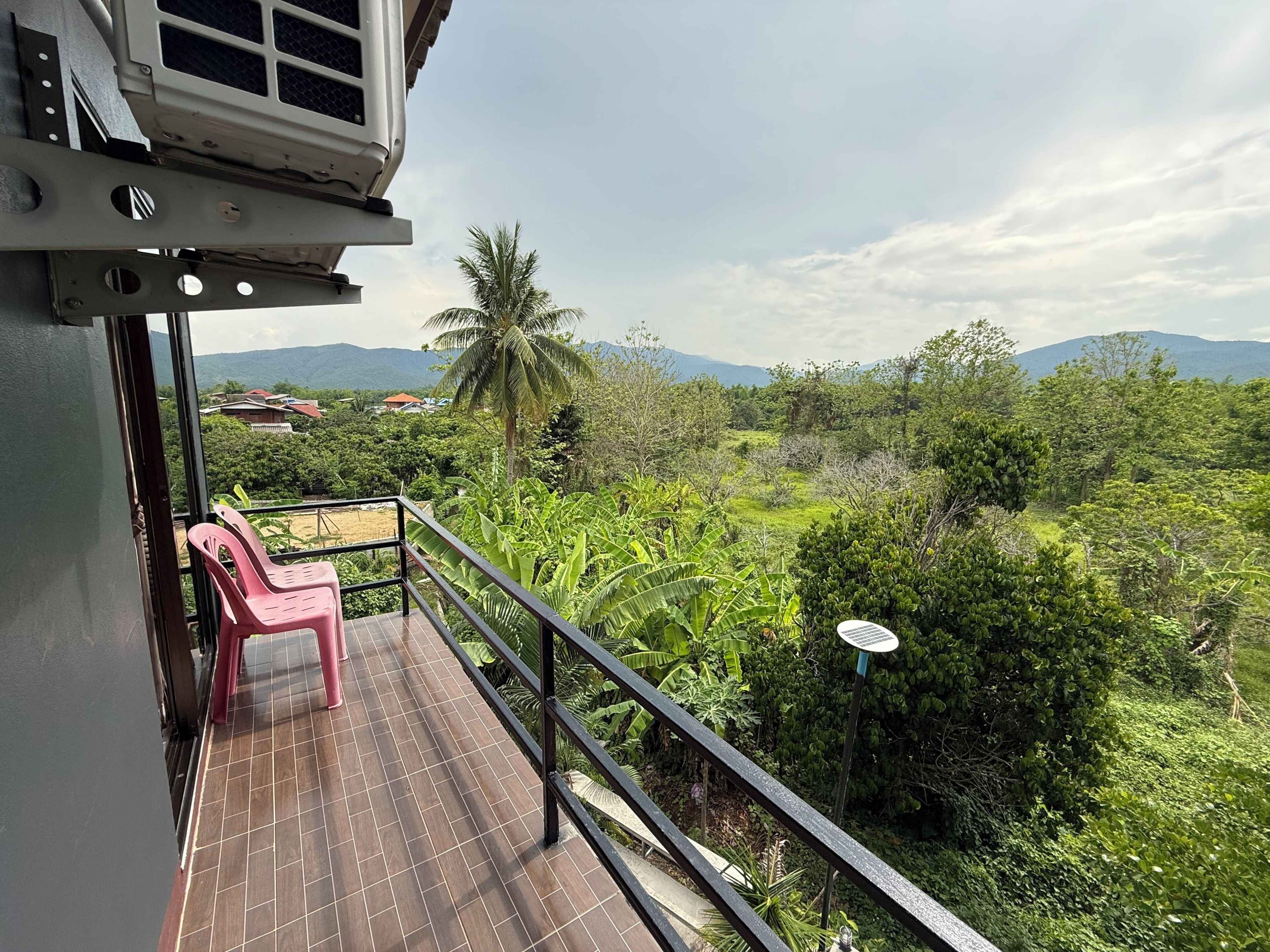 A balcony with a view of a lush landscape, including trees and distant mountains.