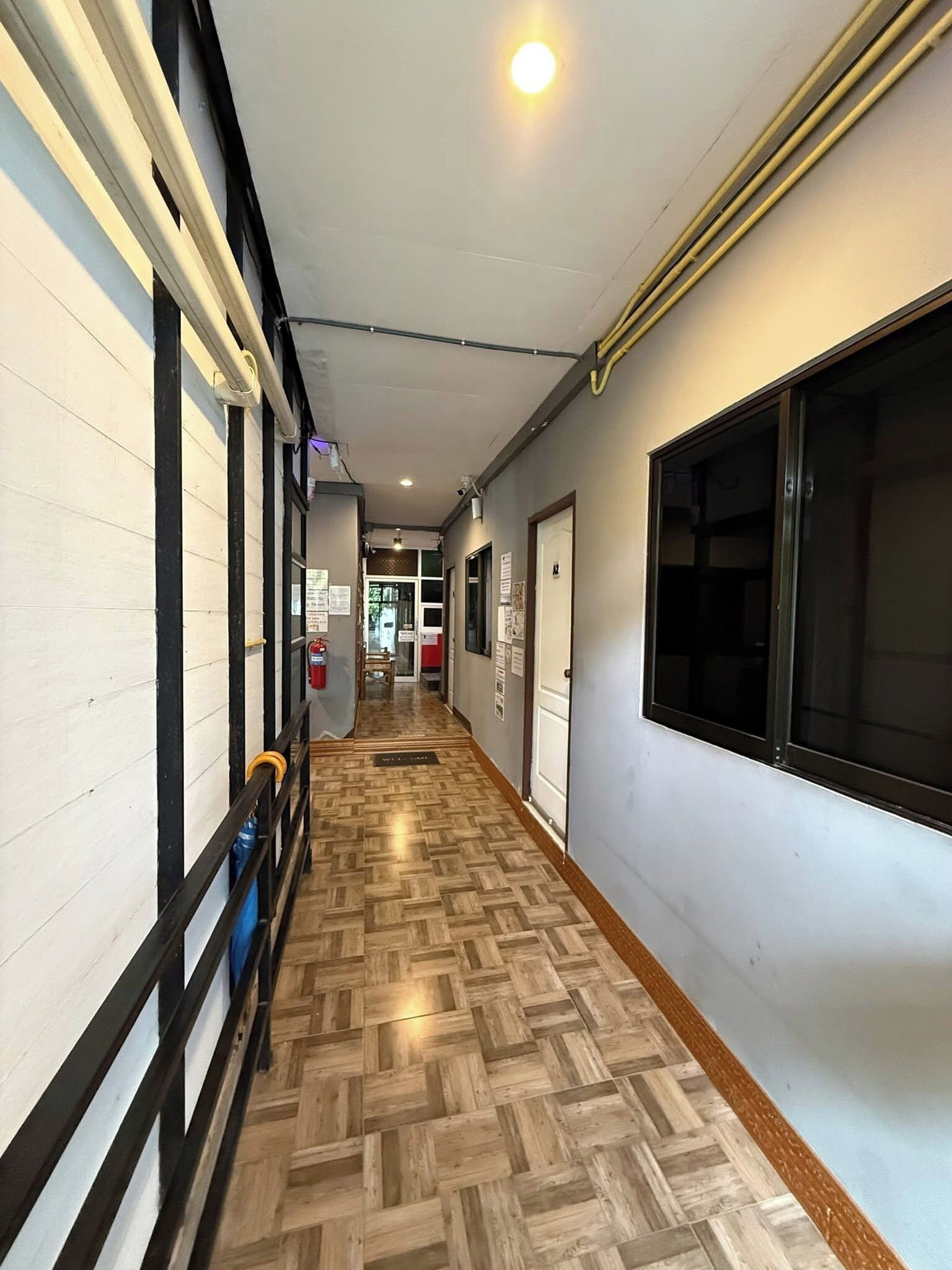 A hallway with a wooden parquet floor, white walls, and a black-framed window.