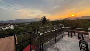 A rooftop terrace with a view of the sunset, a palm tree, and distant mountains. - Sandee Place Mountain View Chomthong (Chom Thong)
