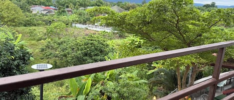Un balcón con vistas a un paisaje verde exuberante, un panel solar y una cadena montañosa distante.