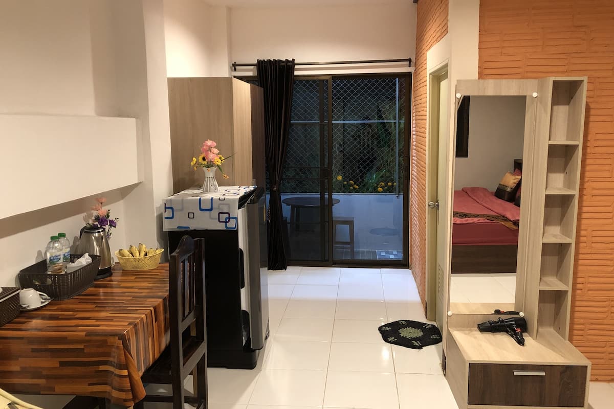 A compact living space with a dining table, a small kitchenette, a sliding glass door leading to an outdoor area, and a wardrobe with shelves.
