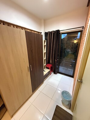 A room with a sliding glass door leading to an outdoor area, a wooden wardrobe, a small stool, and a tiled floor. - Sandee Place Mountain View Chomthong (Chom Thong)
