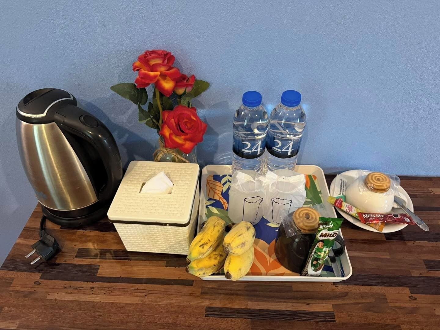 A tray with a coffee maker, a tissue box, two water bottles, bananas, a jar of jam, a packet of milk, and a plate with a pastry.