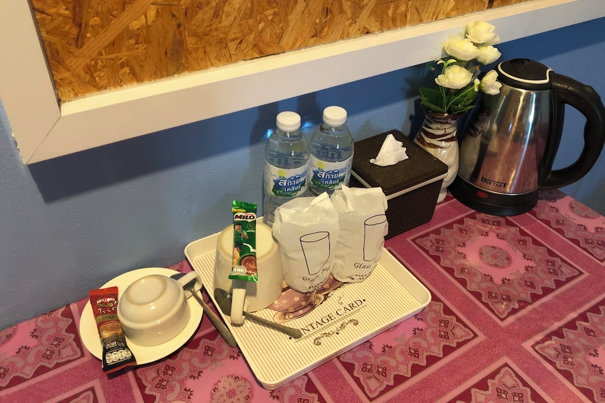A table with a teapot, two bottles of water, a tissue box, a box of tissues, a packet of MILD tea, a cup of tea, a teacup, a teapot, a spoon, a napkin, and a small packet of snacks.
