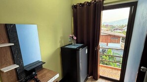 A compact room with a wooden desk, a black refrigerator, and a view through a glass door. - Sandee Place Mountain View Chomthong (Chom Thong)