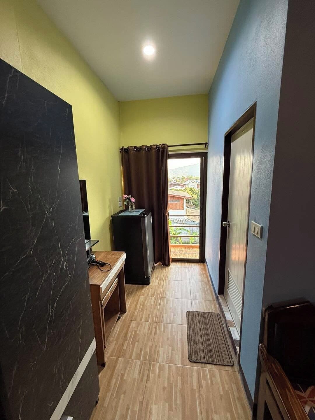 A narrow hallway with a wooden floor, a small table with a chair, a black cabinet, and a door leading to an outdoor area.