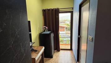 A narrow hallway with a wooden floor, a small table with a chair, a black cabinet, and a door leading to an outdoor area.