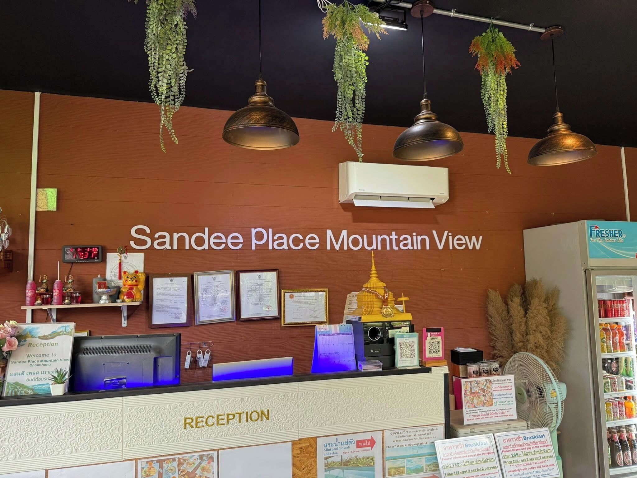 A reception desk with a sign reading 'Sande Place Mountain View,' a computer, framed certificates, and a small Buddha statue.