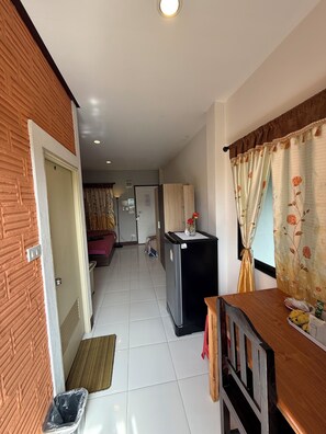 Un pasillo que da a un dormitorio con una puerta, un refrigerador y una mesa con un florero y plátanos.