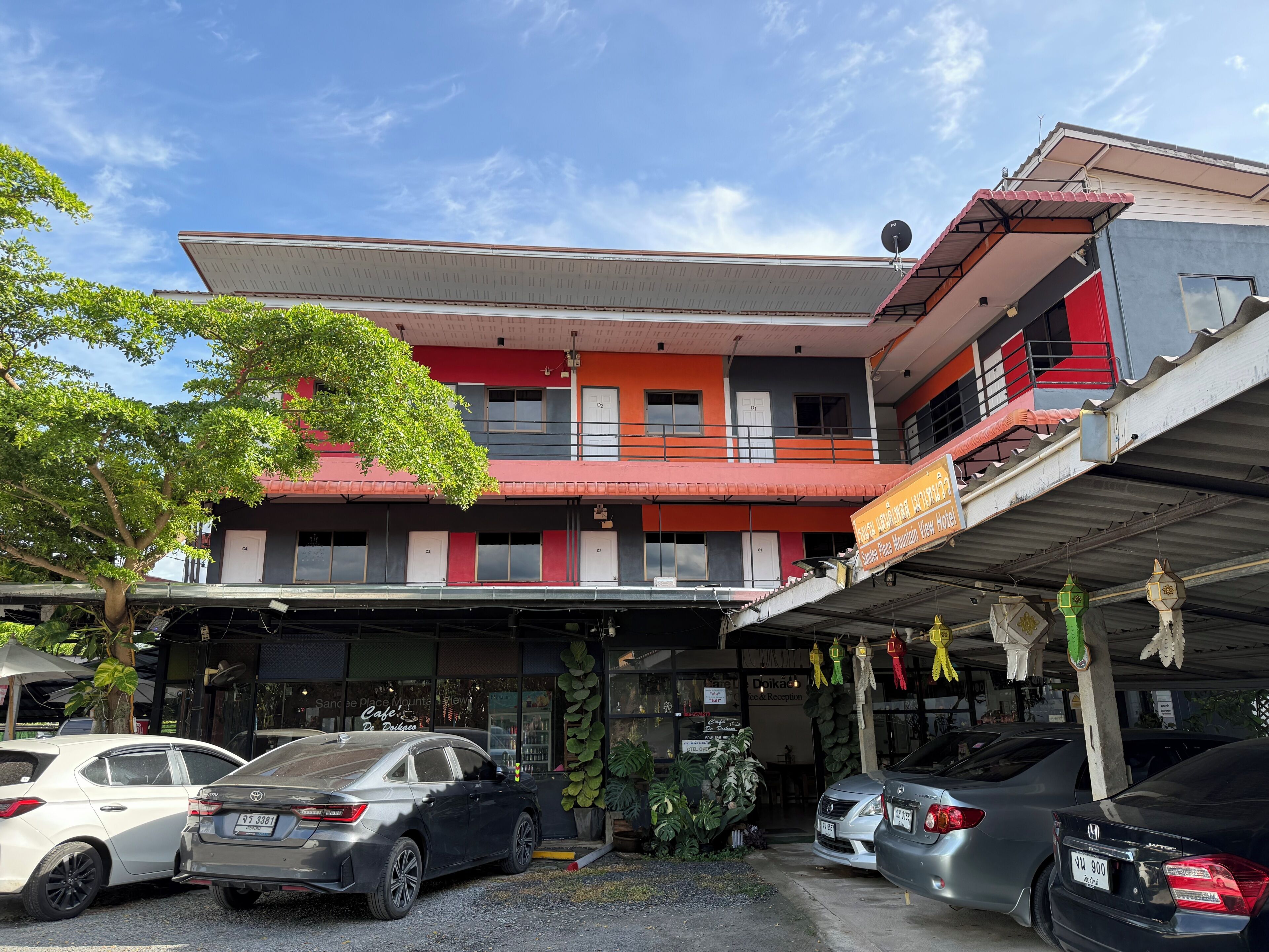 A multi-story hotel with a red and grey facade, a covered parking area, and several parked cars.