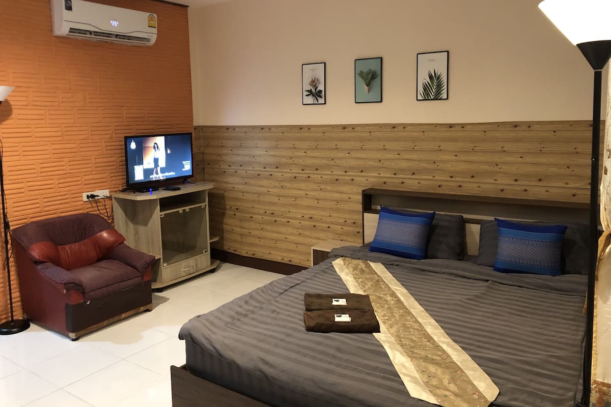 A hotel room with a bed, a television, a chair, and a wall-mounted air conditioner.