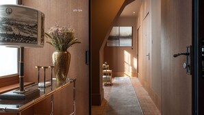 A hallway with a wooden floor, a glass display case with a vase of flowers, and a wall-mounted lamp. - Cour des Vosges - Evok Collection (Paris)