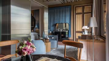 A modern hotel room with a round dining table, a vase of flowers, a sofa, a coffee table, and a large mirror.