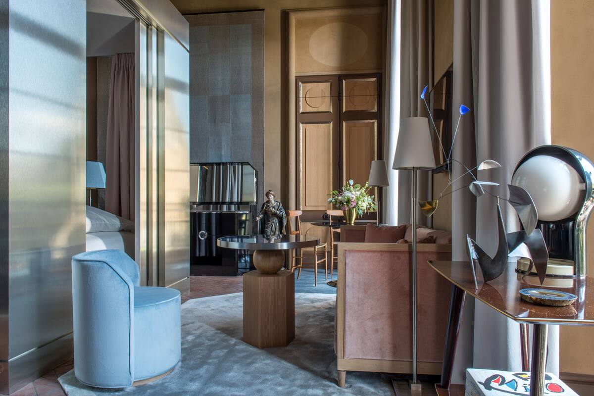 A modern hotel room with a sofa, a round table, a lamp, and a decorative mirror.