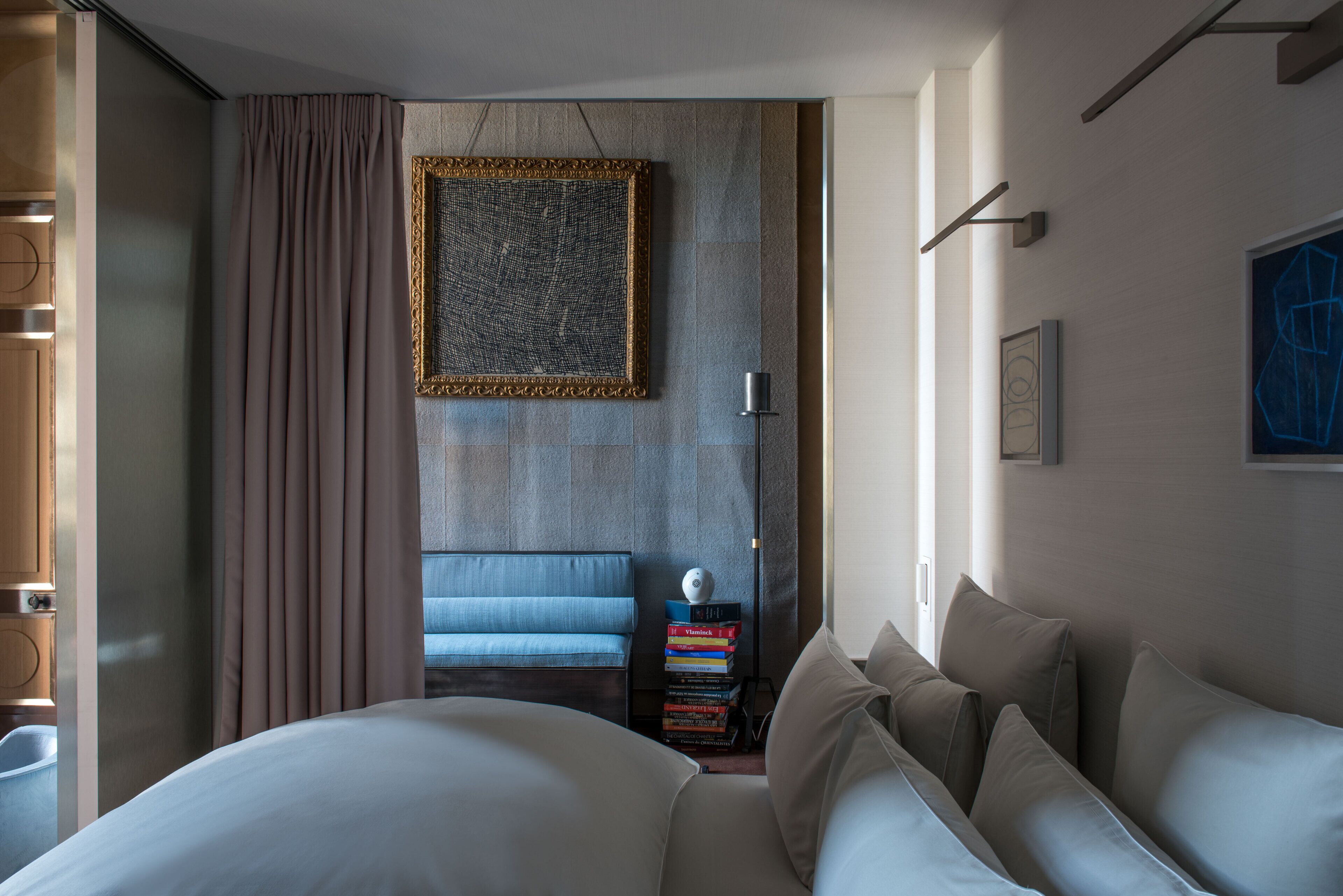 Une chambre d’hôtel moderne avec un grand lit, un canapé bleu, une pile de livres et une œuvre d’art encadrée accrochée au mur.