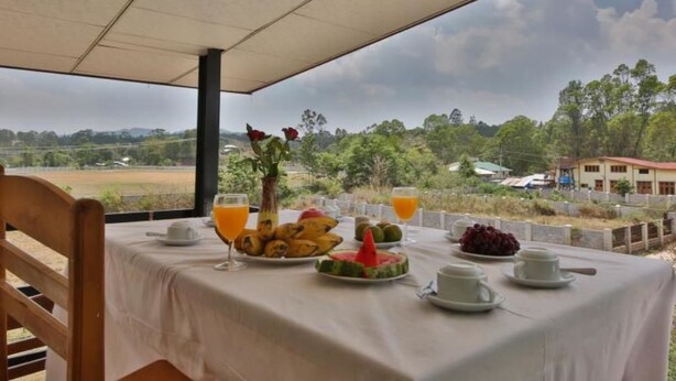 A table set for breakfast with fruit, juice, and cups, overlooking a scenic landscape. - Railroad Hotel Kalaw (Kalaw)