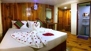 A hotel room with a wooden headboard, a bed with rose petals and a swan towel arrangement, a small table with a mirror, and a bathroom visible through an open door. - Railroad Hotel Kalaw (Kalaw)