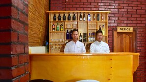 A bar area with a brick wall, a wooden counter, and shelves with bottles and glasses. - Railroad Hotel Kalaw (Kalaw)