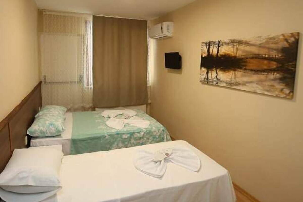 A hotel room with two beds, a painting on the wall, and a window with curtains.