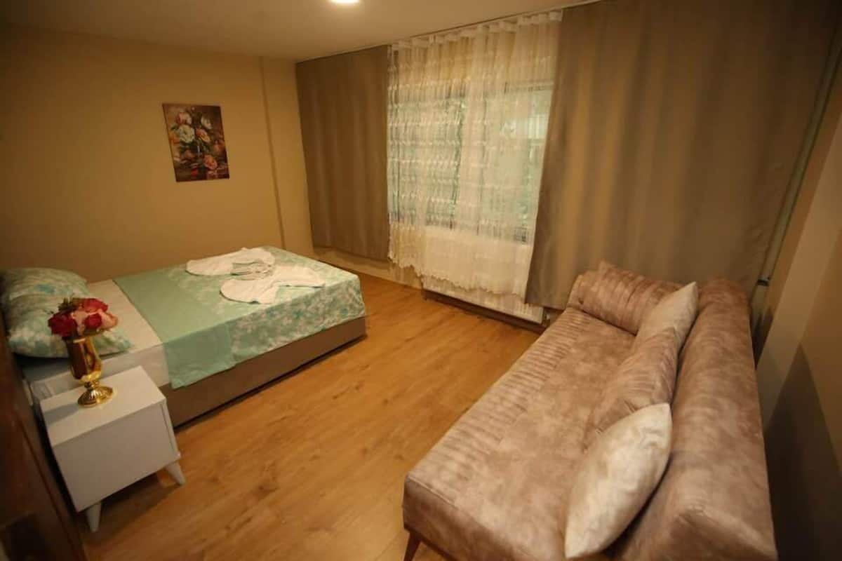 A bedroom with a bed, a sofa, a nightstand, a vase with flowers, and a painting on the wall.