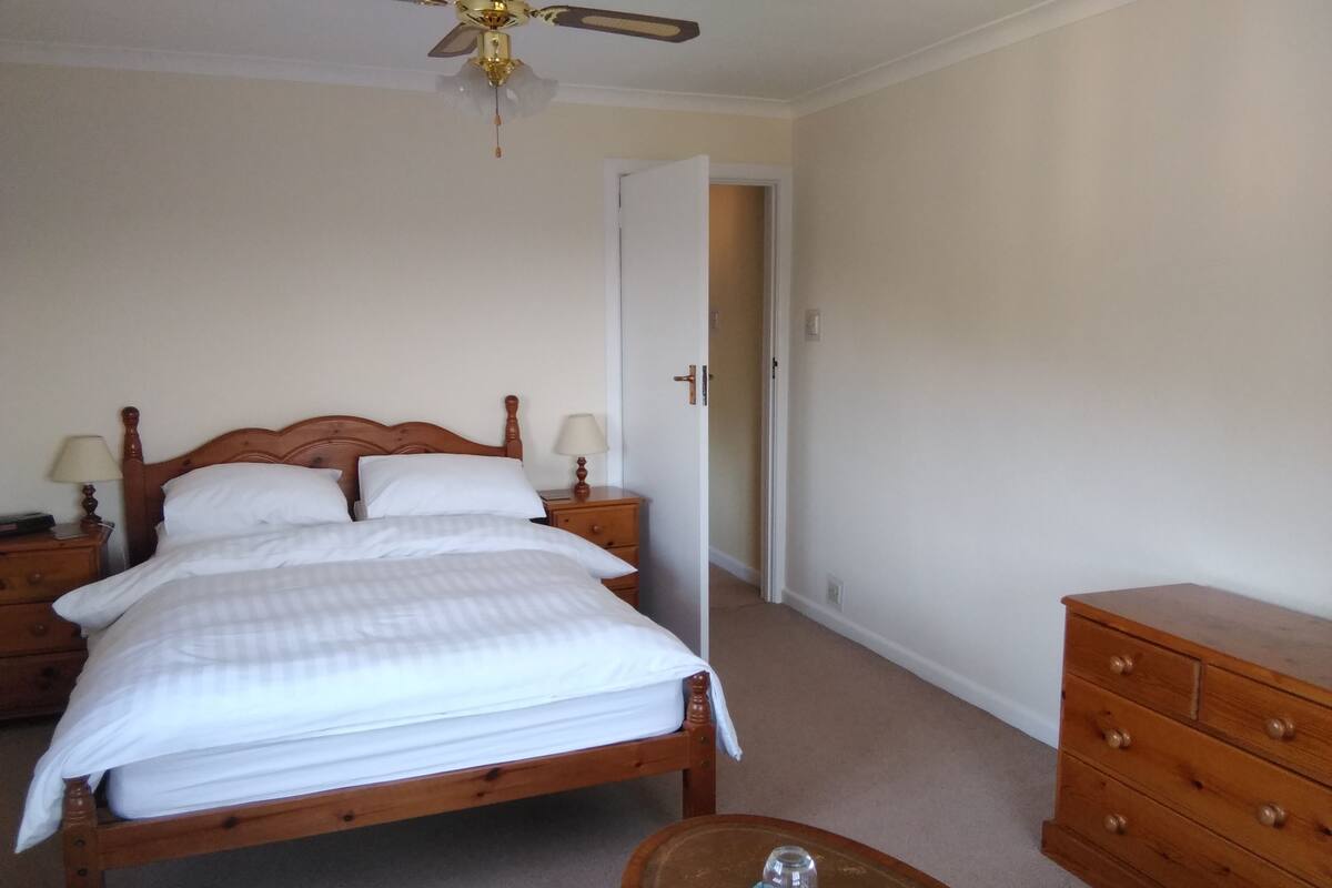 A neatly made bed with a wooden headboard, two bedside tables with lamps, a wooden dresser, and a ceiling fan.