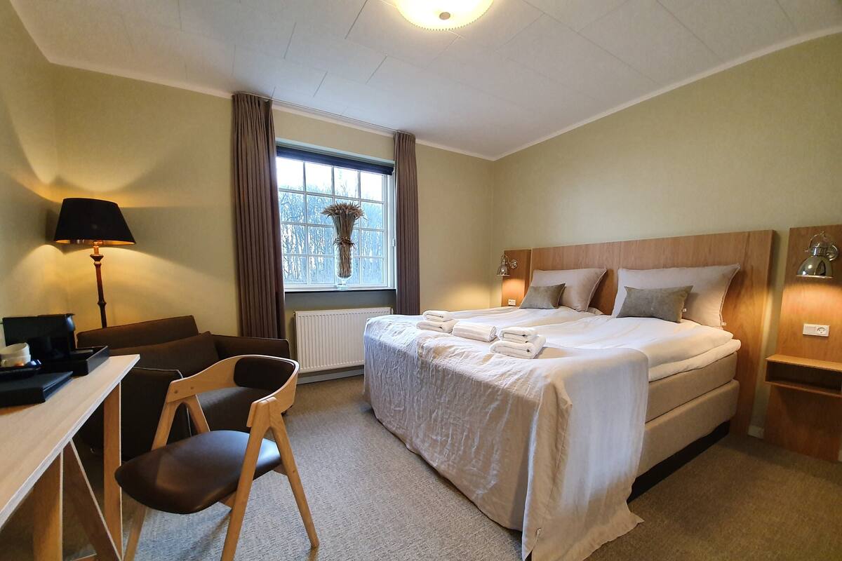 A hotel room with a bed, a desk, a chair, a lamp, and a window with curtains.