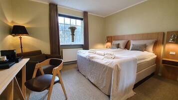 A hotel room with a bed, a desk, a chair, a lamp, and a window with curtains.