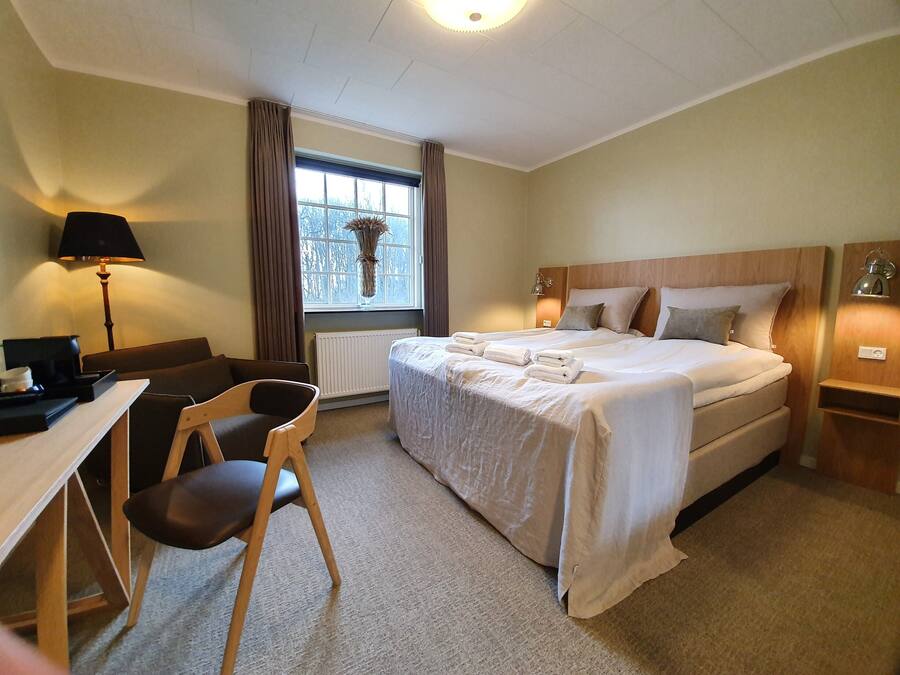 A hotel room with a bed, a desk, a chair, a lamp, and a window with curtains.