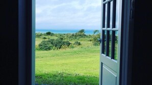 A door leading to a view of a grassy field and the ocean. - Hotel Nor - Badehotellet (Fjerritslev)