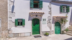 A building with a white facade, green shutters, and a central green door. - 1 bedroom nice home in Lubenice (Lubenice)