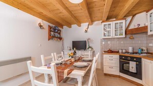 A cozy kitchen with white cabinets, a wooden ceiling, and a dining area with white chairs and a table set for four. - 1 bedroom nice home in Lubenice (Lubenice)