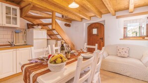A cozy kitchen with wooden beams, a dining table set with plates, glasses, and a fruit basket. - 1 bedroom nice home in Lubenice (Lubenice)