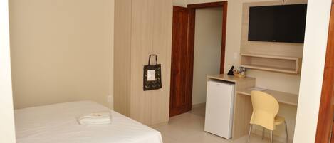 Una habitación de hotel con cama, escritorio, silla, televisor y minibar.