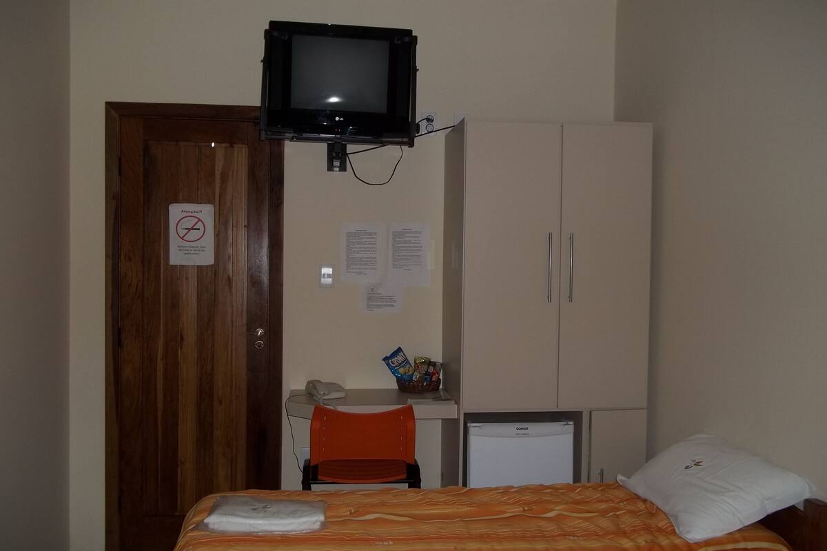 Quarto de hotel com cama, televisão na parede, secretária com cadeira e frigorífico.