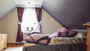 Une chambre avec un plafond en pente, un lit recouvert d’une couvre-lit à motifs et une fenêtre avec des rideaux.