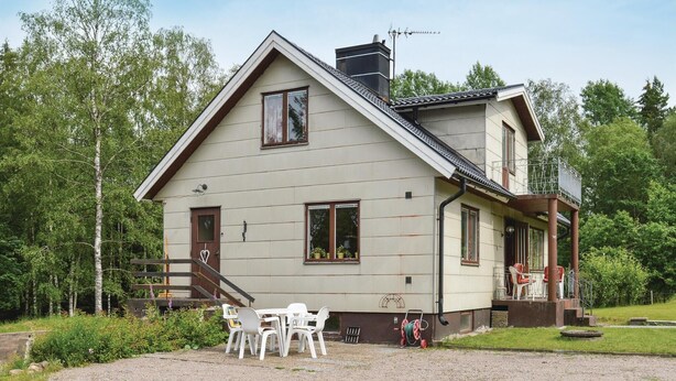 Une maison à deux étages avec un toit en pente, un porche à l’avant doté de sièges extérieurs et une allée gravillonnée.