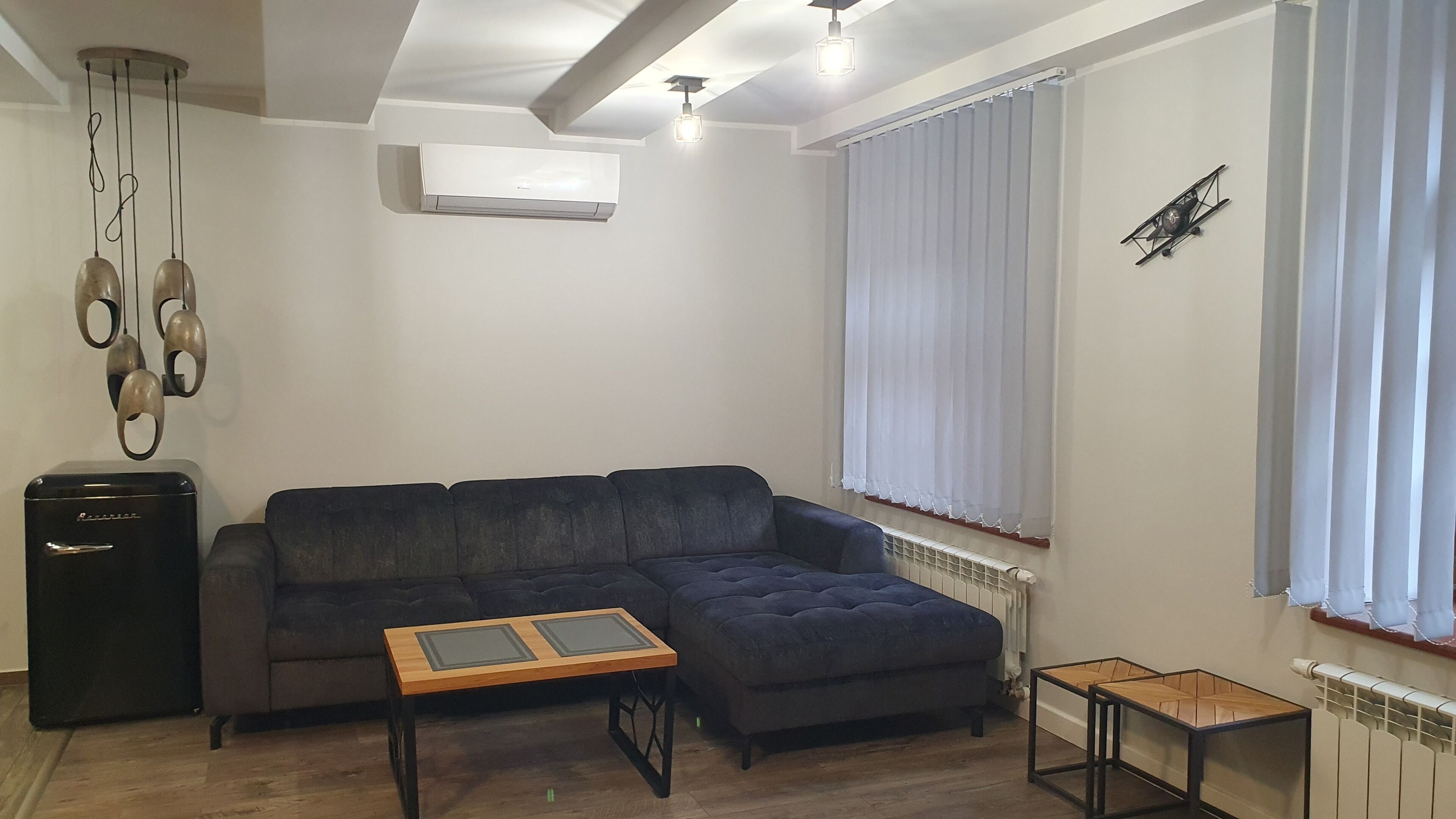 Una sala de estar con un sofá seccional, una pequeña mesa de madera, un radiador y un ventilador de techo.