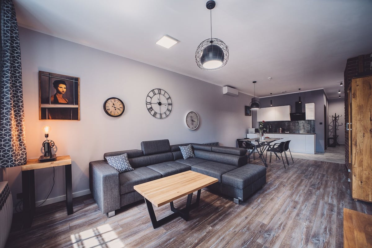 A modern living room with a sectional sofa, a wooden coffee table, and two wall clocks.