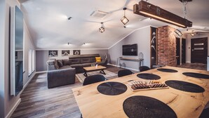 Ein geräumiger Wohnbereich mit einem Holzessttisch, einer Couch und einem an der Wand befestigten Fernseher.