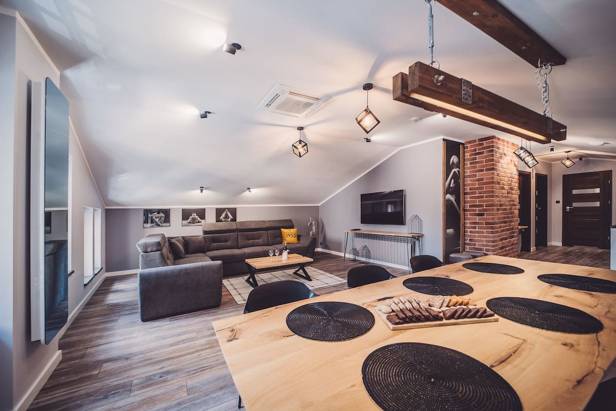 A spacious living area with a wooden dining table, a sofa, and a TV mounted on the wall.